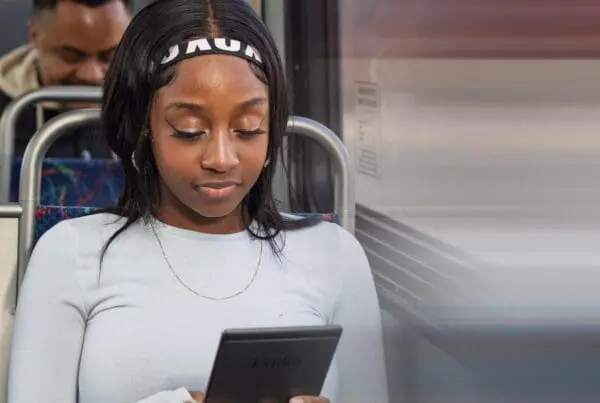 Young woman with a headband reading a Kindle e-reader while sitting on a bus.