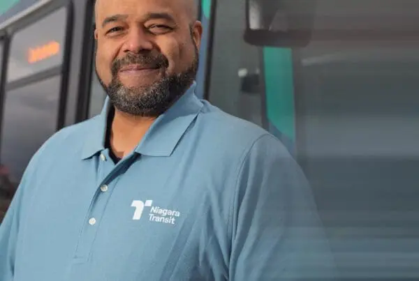 Smiling man wearing a light blue Niagara Transit polo shirt standing in front of a bus.