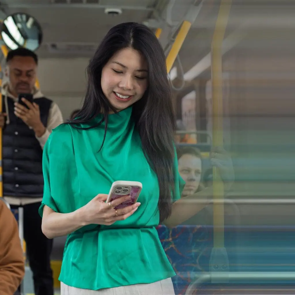 Woman in a green blouse looking at her phone while standing on a bus.