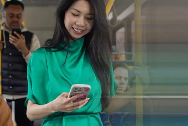 Woman in a green blouse looking at her phone while standing on a bus.
