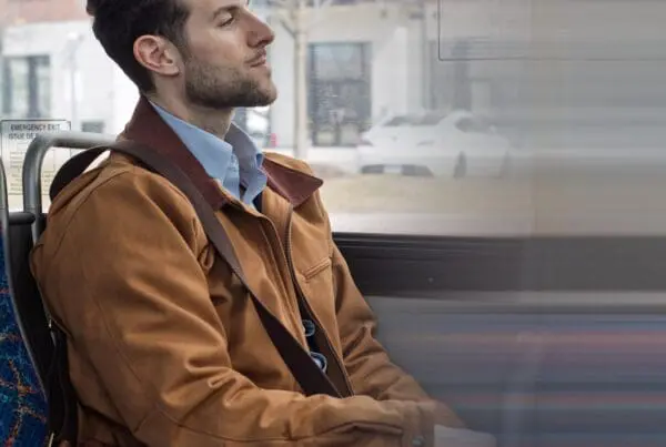 Man with a brown jacket and leather bag sitting on a bus, looking out the window.