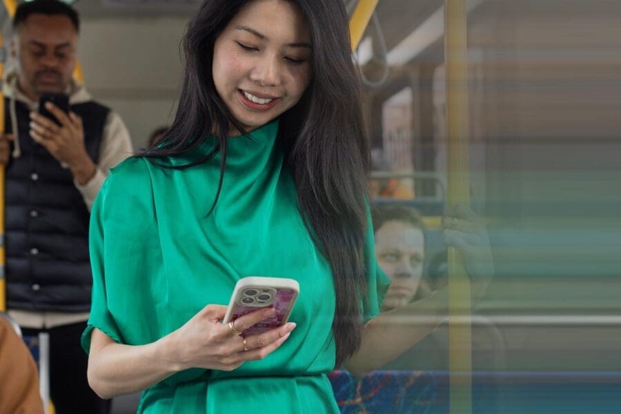 Woman in a green blouse looking at her phone while standing on a bus.